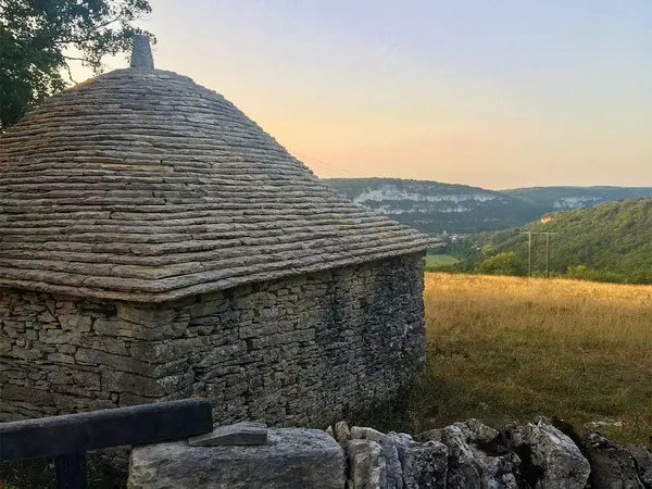 une cazelle dans le quercy, région des gorges de l'aveyron et du rouergue ; on voit le toit de la cazelle, en lauzes calcaires et au loin un pré qui invite à la marche