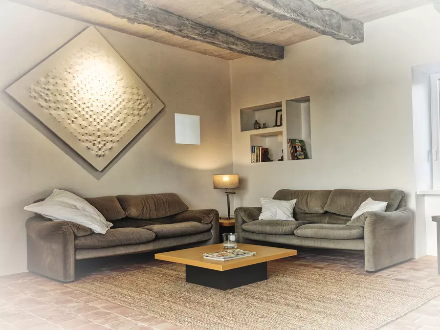 le salon de la cubane, gite en occitanie, avec les deux canapés , la table basse en bois, un tableau style castellani sur le mur gauche, trois niches sur le mur du fond avec livres et bibelots ; tapis posé sur le sol en tomettes ; un fenestron sur le mur gauche