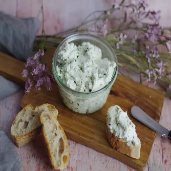 sur une petite planche à découper en bois, du fromage frais de chèvre mélangé à de fines herbes, trois tranches de pain et un couteau arrondi pour étaler le fromage