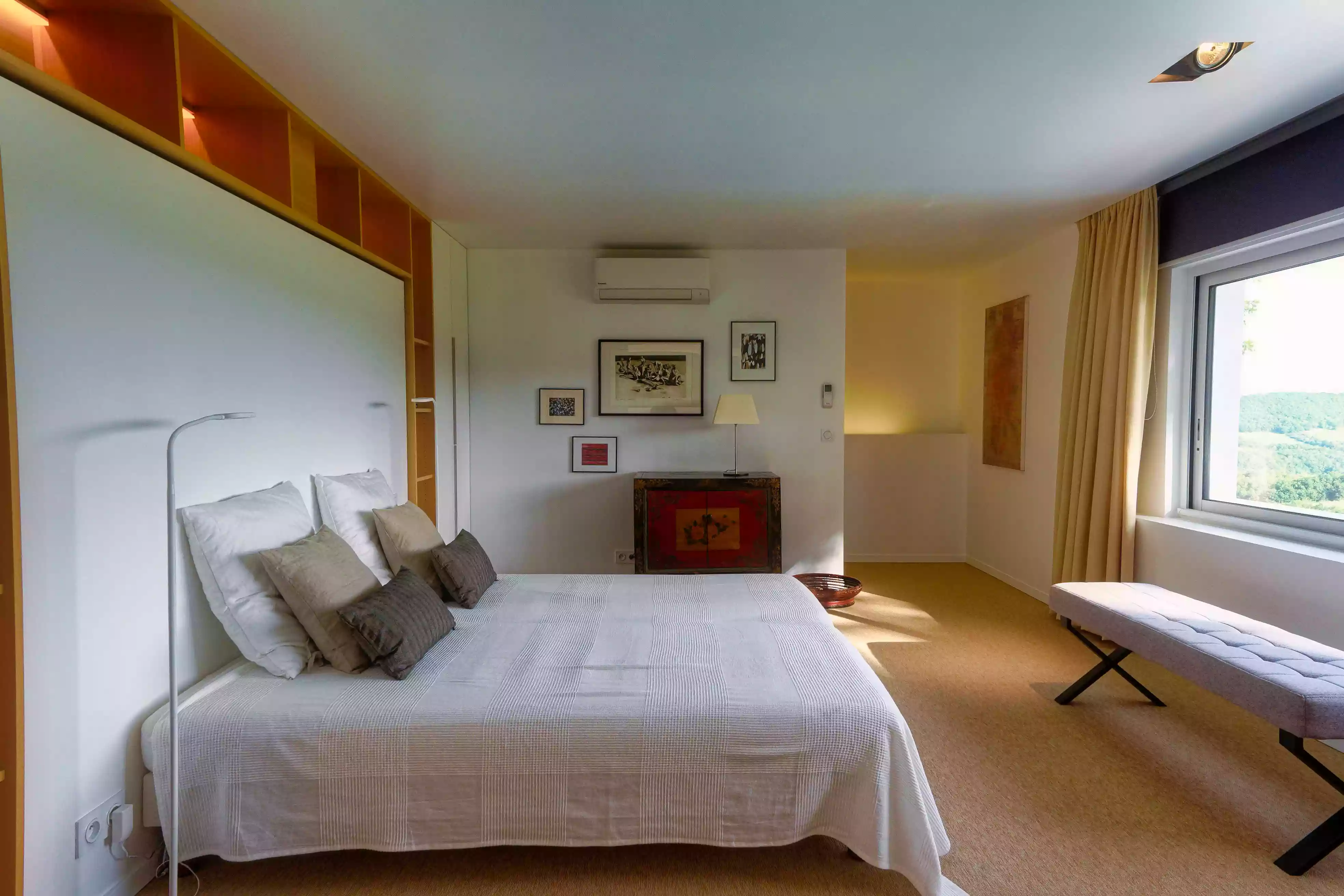 la chambre d'étage du gîte de la cubane à Verfeil sur Seye (Tarn et Garonne, Occitanie) ; le lit double, une banquette devant la fenêtre et en arrière plan un mur décoré et le départ de l'escalier