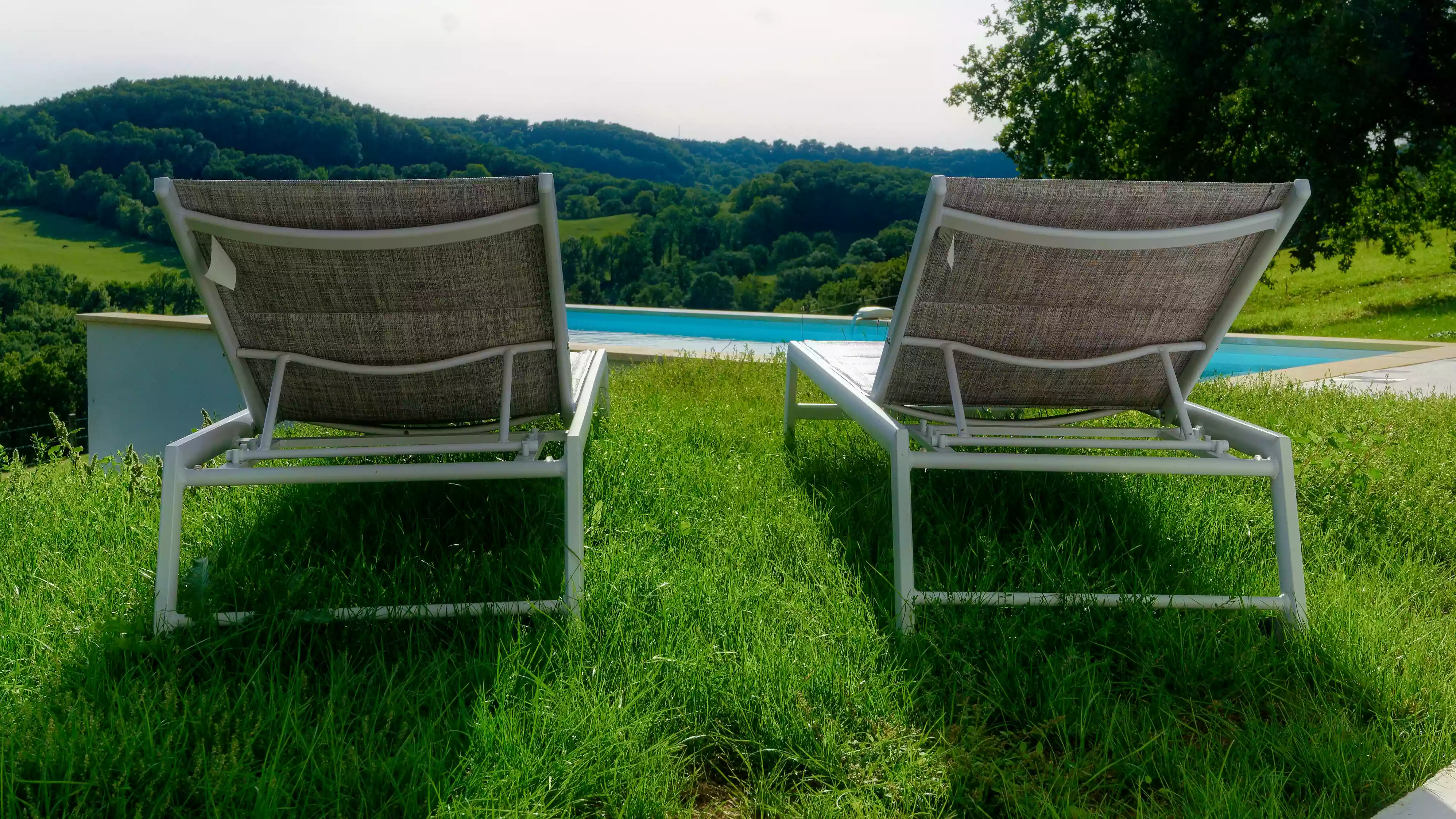 vue sur le paysage environnant du gîte de la cubane à Verfeil sur Seye (Tarn et Garonne, Occitanie), avec les côteaux et les collines vallonées ; en premier plan deux transat qui incitent au repos.