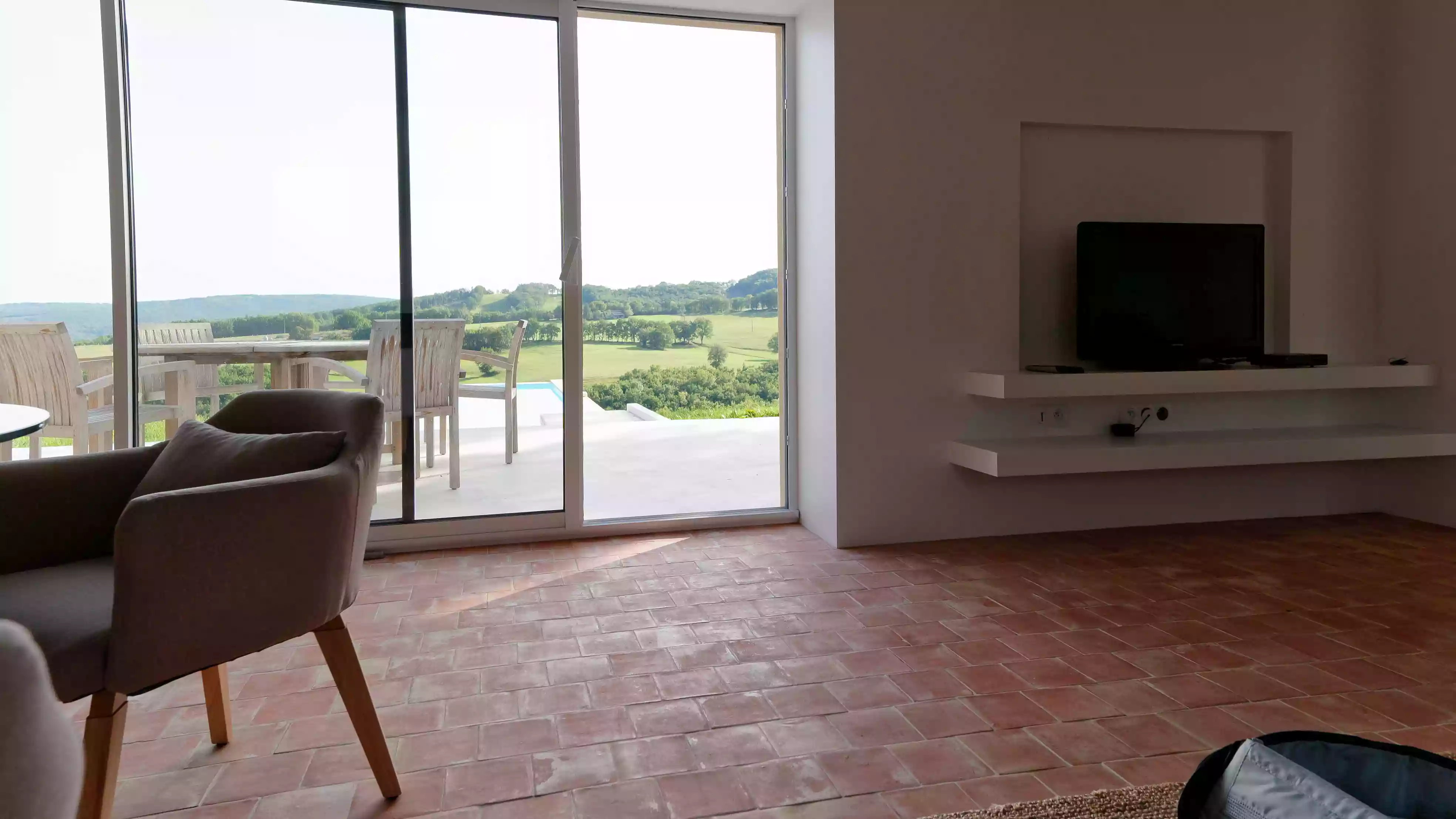 vue sur les collines environnantes depuis le salon de la cubane ; en arrière plan, les vallons et les côteaux du causse du Quercy ; en premier plan, l'intérieur associant contemporain et architecture traditionnelle