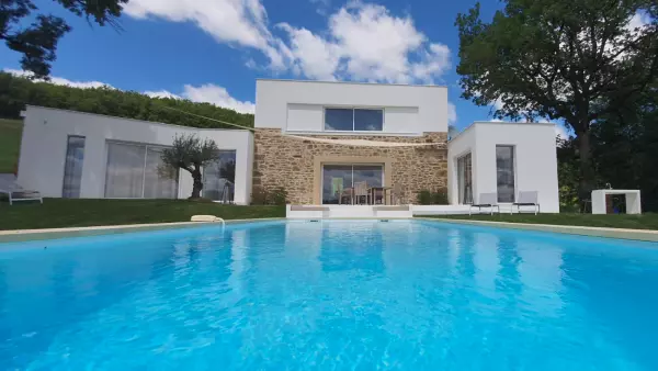 gîte à proximité de Saint-Antonin : la façade contemporaine avec le bloc central et les deux ailes ; en premier plan, la piscine, un olivier en décoration