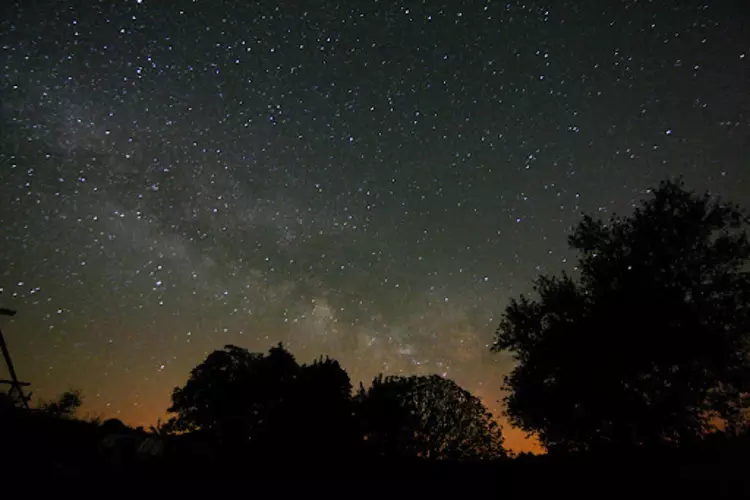 le ciel étoilé avec en arrière plan les rayons du soleil couchant dans le triangle noir des causses du quercy, la zone la moins polluée par les lumières artificielles
