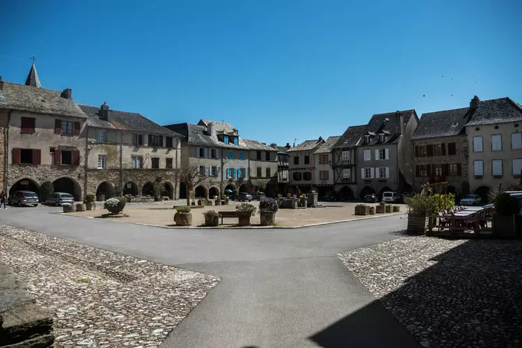 sauveterre de rouergue, bastide de l'aveyron en occitanie ; la grand place avec ses maisons en pierre avec arcades en rez de chaussée ; quelques bancs et plantations sur le pourtour de la place